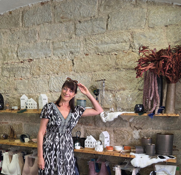 Frau in Modegeschäft vor dekorativer Steinwand mit Accessoires und Kleidung.